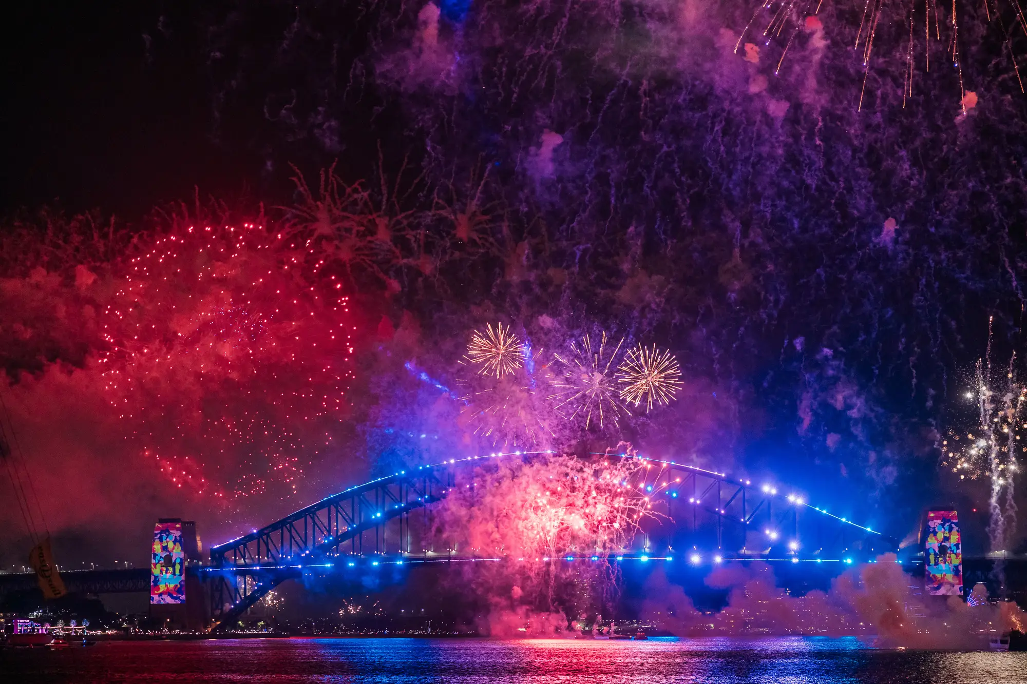 Fireworks over the Sydney Harbour Bridge on New Year's Eve, the Bridge lit blue and the sky red and violet
