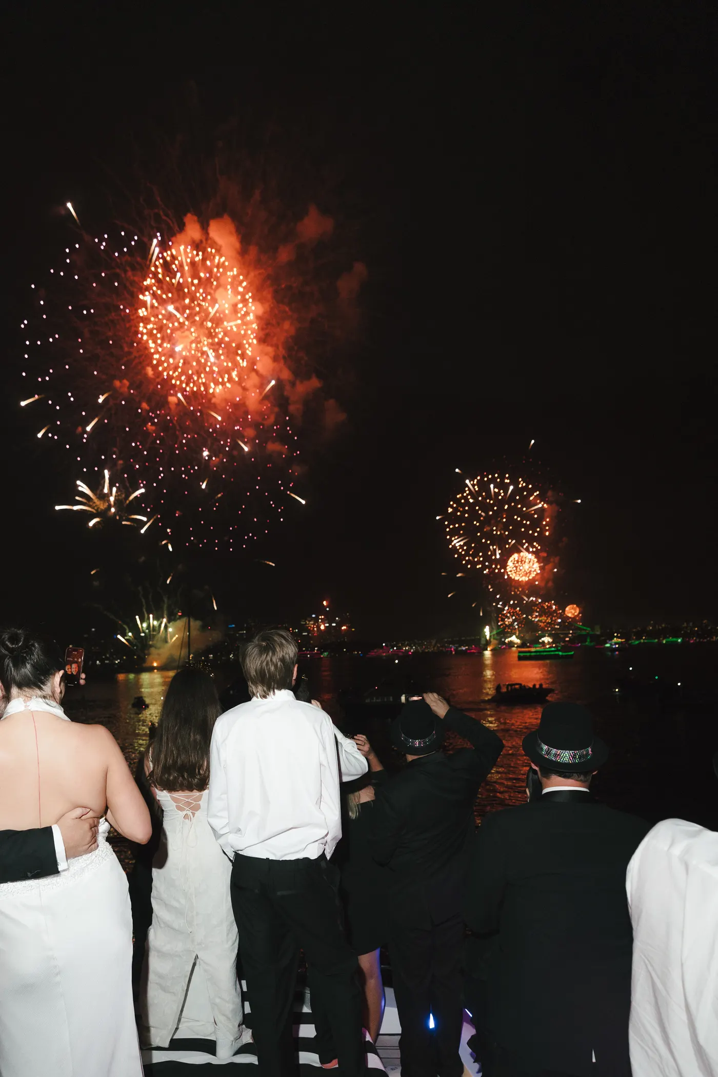 Guests at the rail of a yacht watching red and gold fireworks over the Harbour
