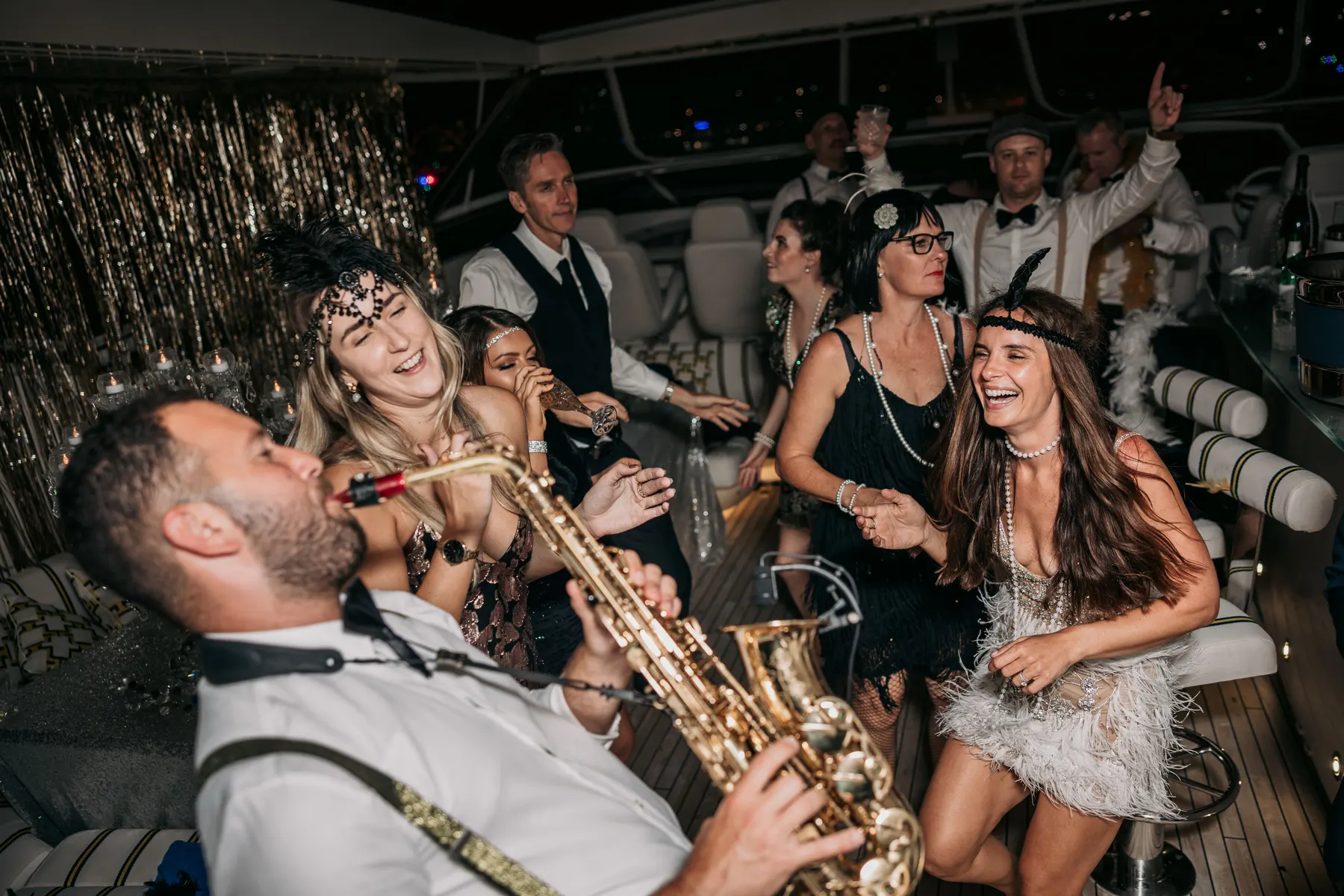Guests dancing and laughing around a saxophonist on the yacht's upper deck