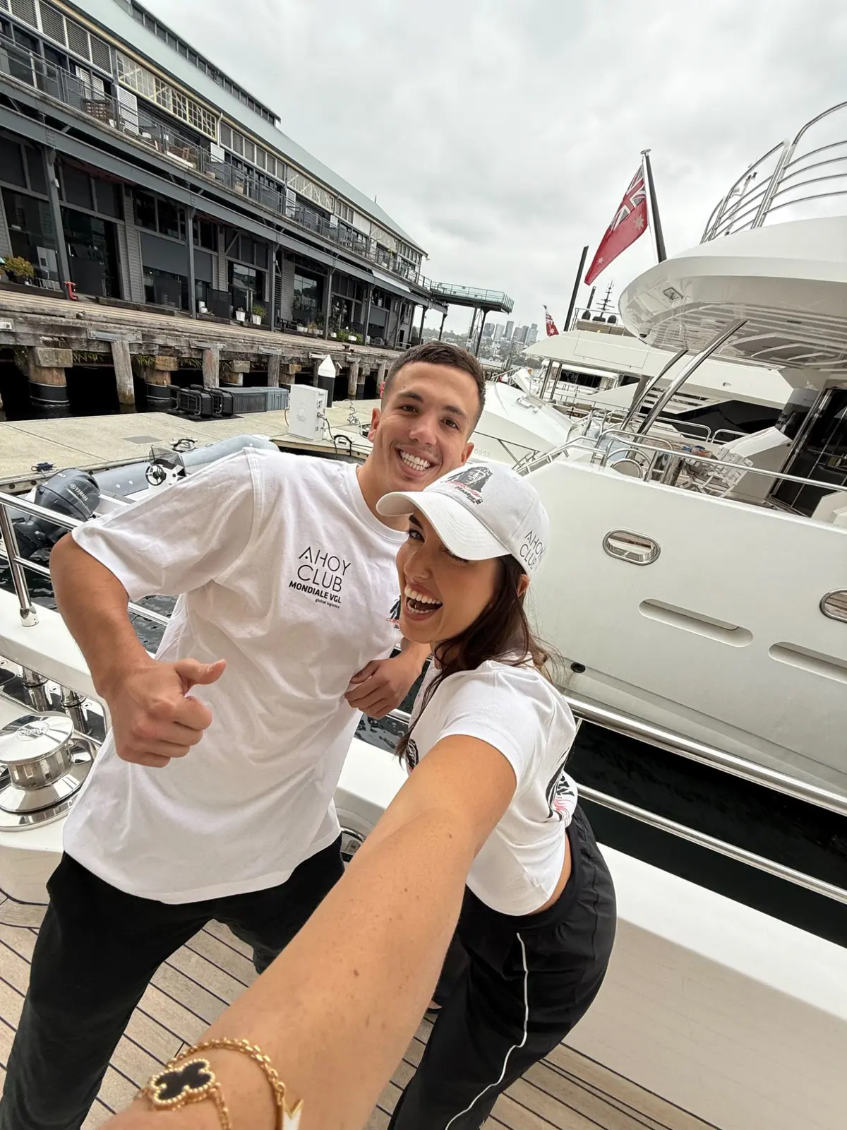 Two of the Ahoy Club team in Comanche shirts and caps on the dock at Sydney Harbour