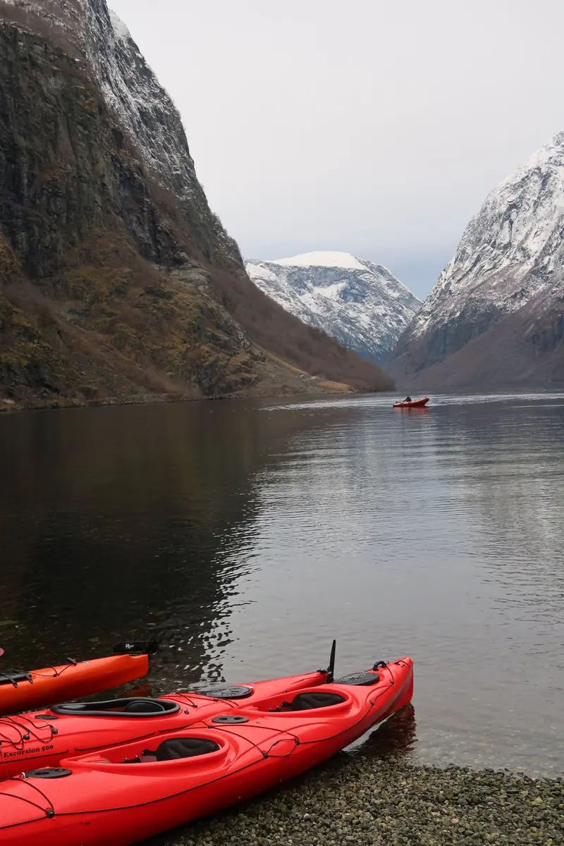 Red canoes pulled up on the shore of the fjord, snowy mountains and a tender on the still water