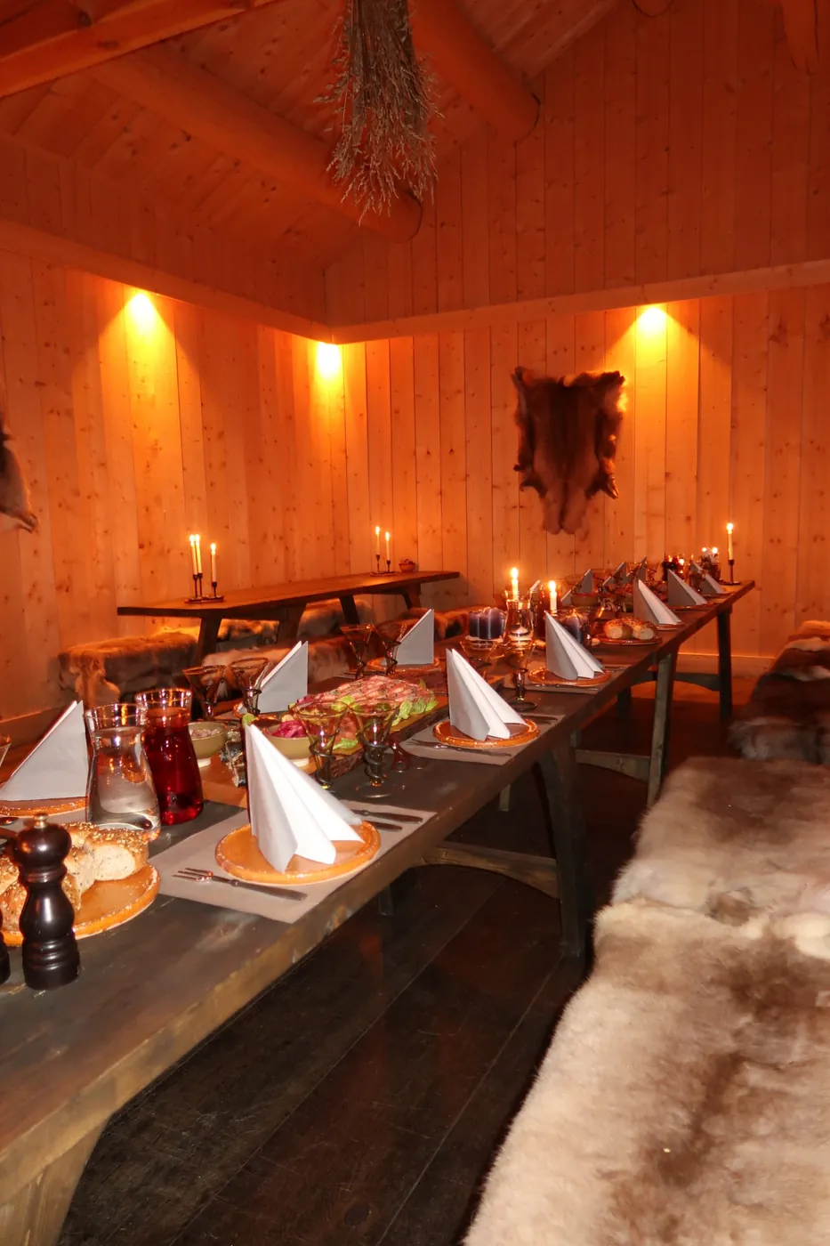 The long table set for the feast in the Viking village hall, candles lit and reindeer skins on the benches